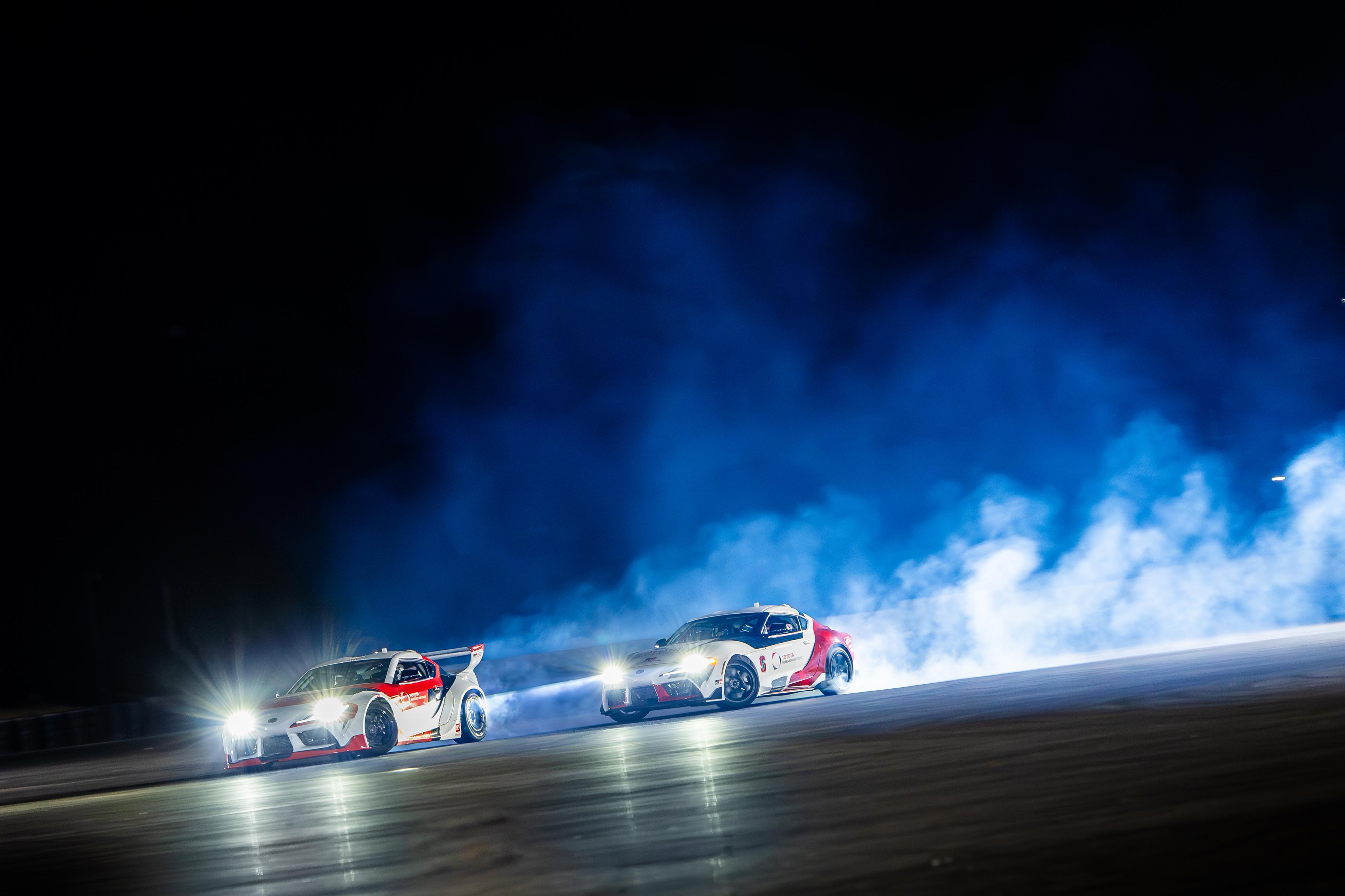 Smoke rises from the tires of autonomously drifting Toyota Supras.